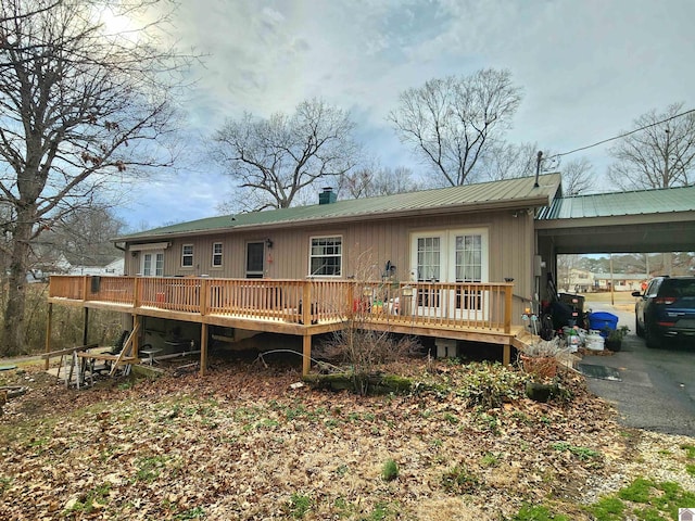 back of house featuring driveway, metal roof, a deck, and a carport