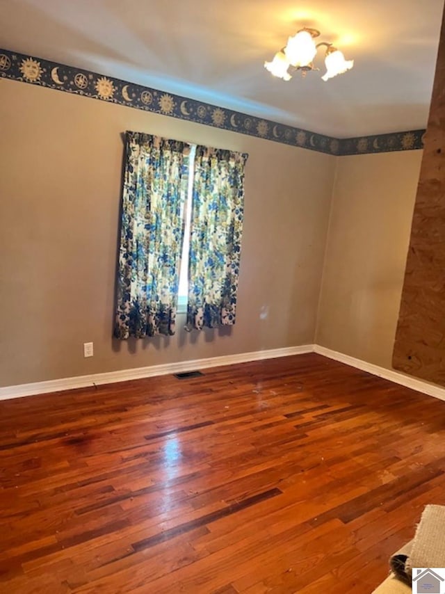 spare room with an inviting chandelier, visible vents, baseboards, and wood finished floors