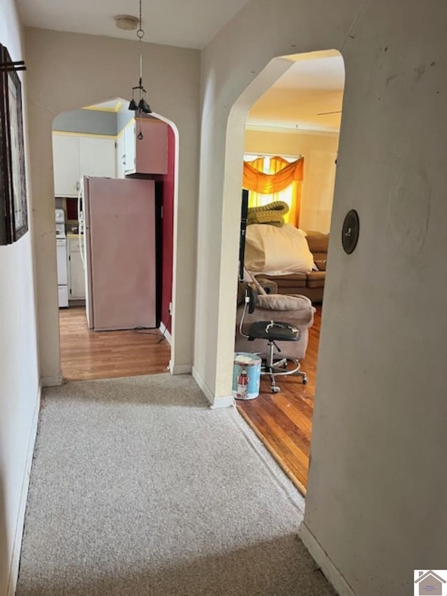 corridor featuring light wood-style floors, baseboards, arched walkways, and light colored carpet