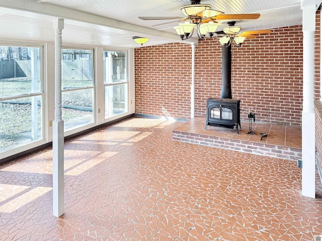 unfurnished living room with a ceiling fan, a wood stove, and brick wall