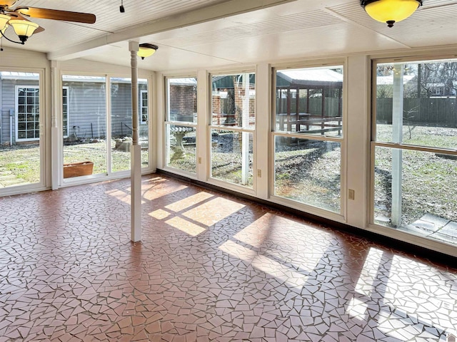 unfurnished sunroom with a healthy amount of sunlight, ceiling fan, and beam ceiling