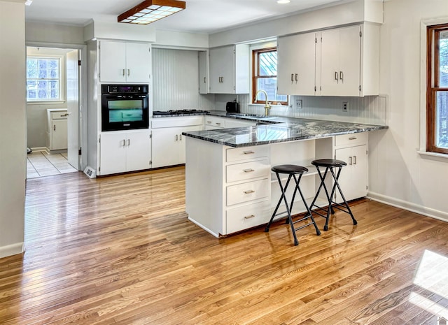 kitchen with dark stone counters, oven, a peninsula, white cabinetry, and a sink