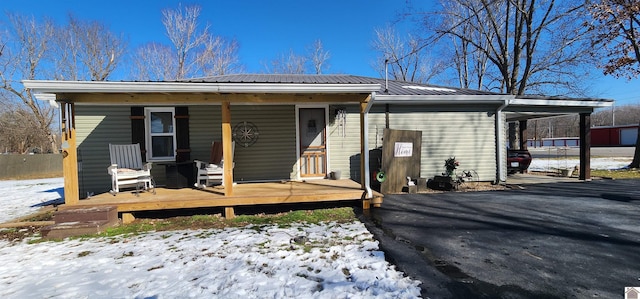 snow covered house with aphalt driveway, fence, metal roof, and an attached carport