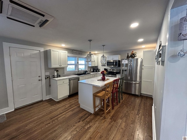 kitchen featuring stainless steel appliances, a sink, white cabinetry, a center island, and decorative light fixtures