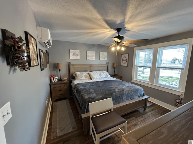 bedroom with a wall unit AC, dark wood finished floors, a ceiling fan, a textured ceiling, and baseboards