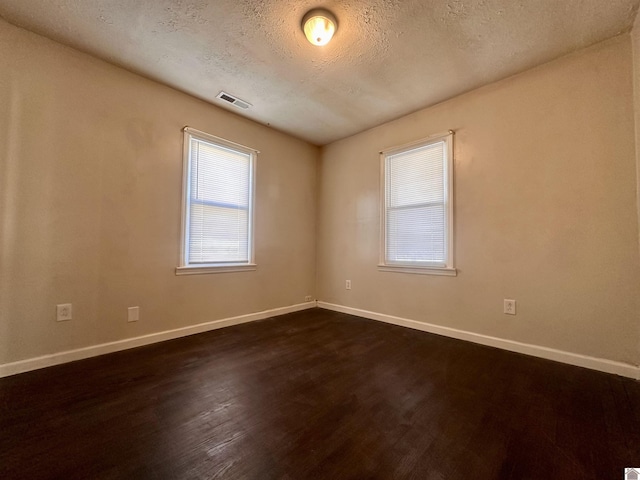 spare room featuring a textured ceiling, dark wood-type flooring, visible vents, and baseboards