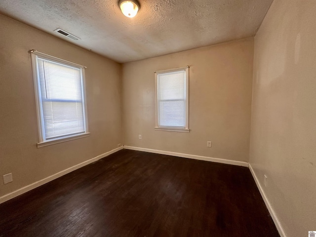 unfurnished room featuring baseboards, visible vents, dark wood finished floors, and a textured ceiling