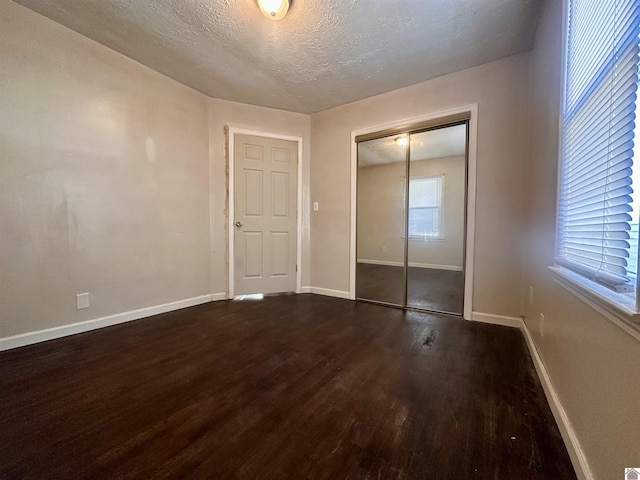 unfurnished bedroom featuring a closet, dark wood finished floors, a textured ceiling, and baseboards