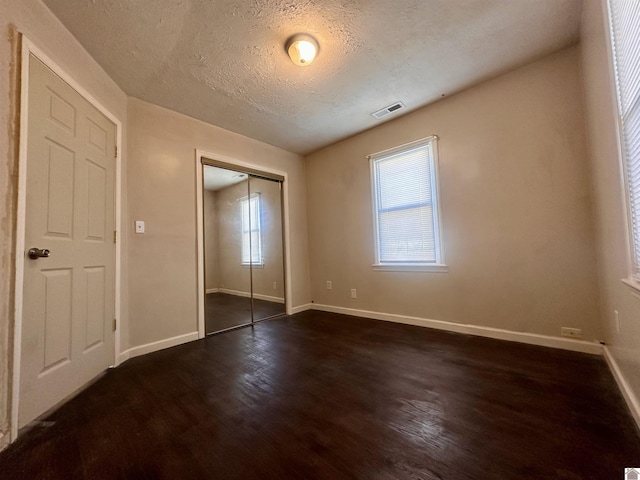 unfurnished bedroom with baseboards, multiple windows, visible vents, and dark wood-type flooring