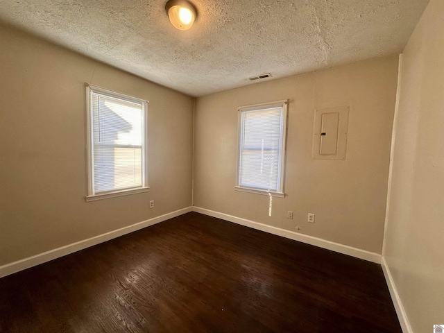 empty room featuring electric panel, baseboards, visible vents, dark wood-style floors, and a textured ceiling