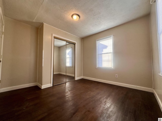 unfurnished bedroom featuring dark wood-type flooring, a closet, a textured ceiling, and baseboards