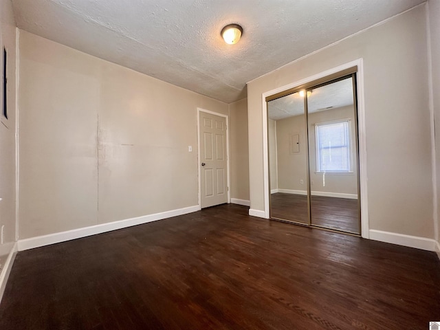 unfurnished bedroom with dark wood-style floors, a closet, baseboards, and a textured ceiling