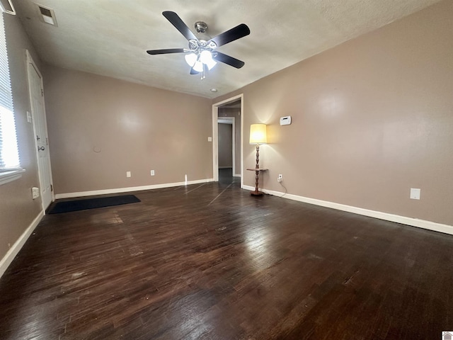 empty room with visible vents, dark wood-style flooring, a ceiling fan, and baseboards