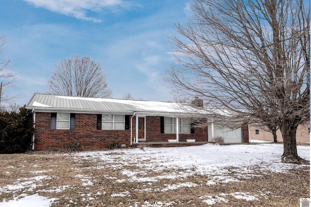 ranch-style home featuring a garage, a chimney, brick siding, and metal roof