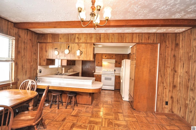 kitchen with a sink, white appliances, brown cabinetry, light countertops, and a chandelier