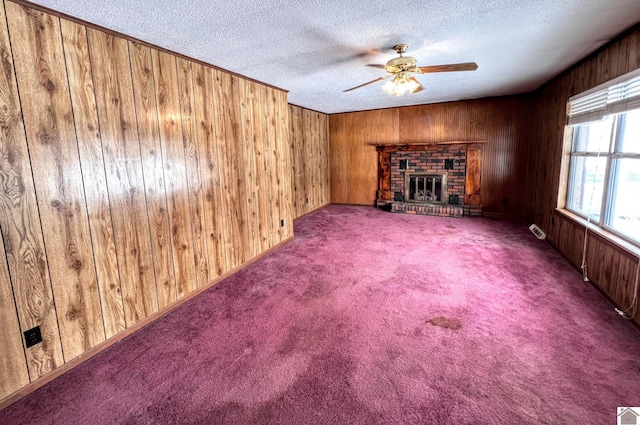 unfurnished living room featuring a ceiling fan, wood walls, carpet flooring, and a textured ceiling