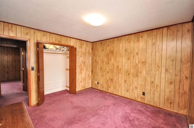 unfurnished bedroom featuring a textured ceiling, a closet, wood walls, carpet flooring, and baseboards