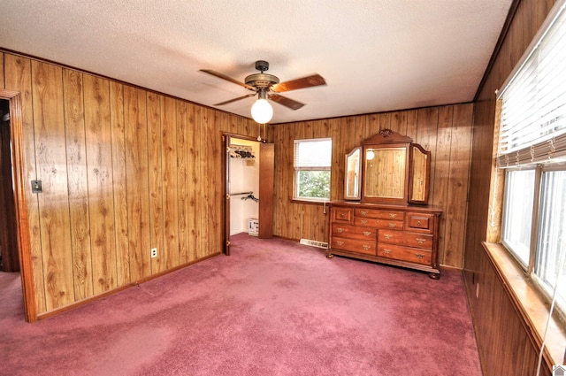 unfurnished bedroom with visible vents, a ceiling fan, a textured ceiling, wooden walls, and dark colored carpet