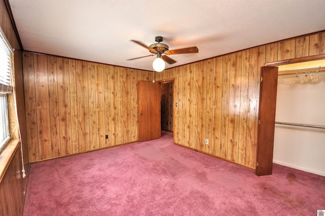 unfurnished bedroom featuring carpet, wood walls, a closet, a textured ceiling, and a ceiling fan