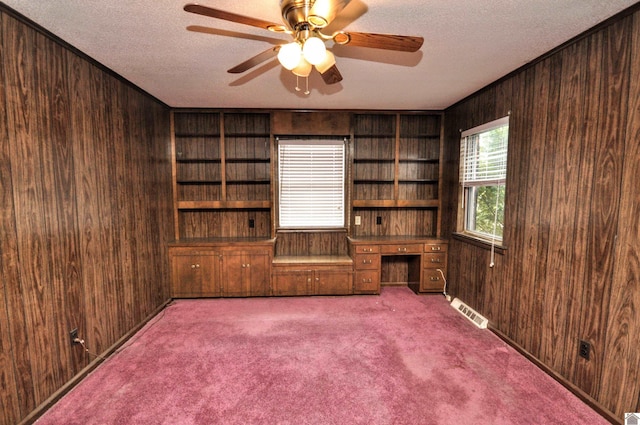 carpeted spare room with a textured ceiling, visible vents, wooden walls, and built in study area