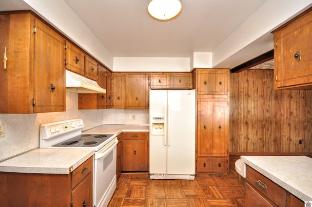 kitchen with brown cabinets, under cabinet range hood, backsplash, white appliances, and light countertops