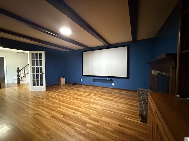 home theater with french doors, a fireplace, beamed ceiling, and light wood-style flooring