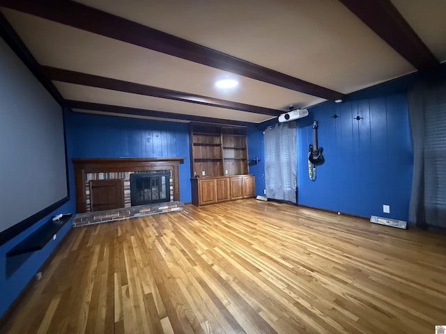 unfurnished living room with beamed ceiling, a brick fireplace, and wood finished floors