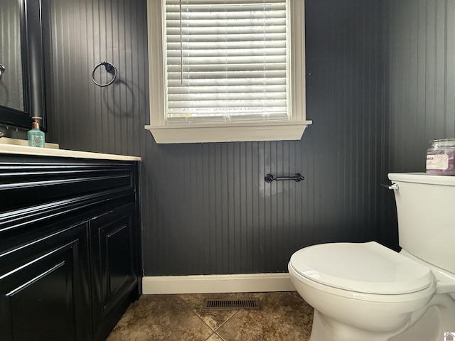 half bath featuring toilet, vanity, visible vents, and baseboards