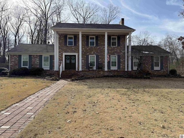 greek revival house with brick siding, a chimney, and a front yard