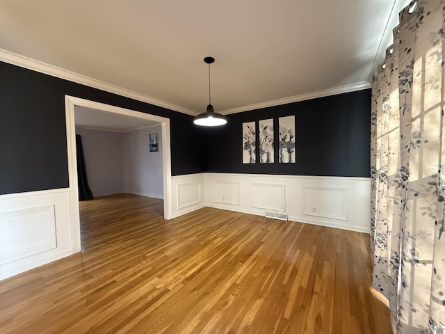 unfurnished dining area featuring ornamental molding, wainscoting, visible vents, and wood finished floors