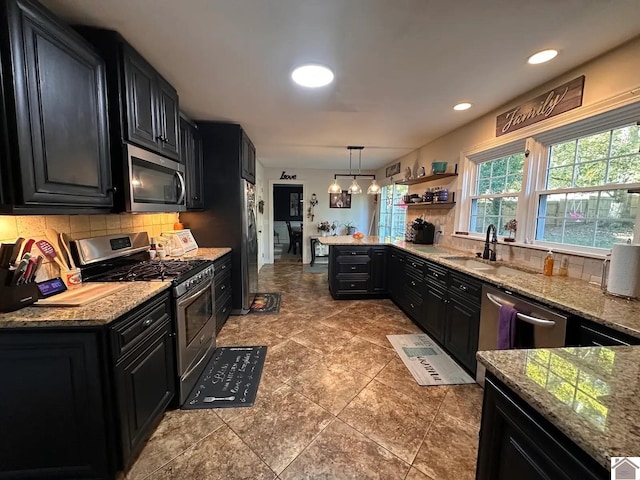 kitchen featuring tasteful backsplash, appliances with stainless steel finishes, dark cabinetry, and decorative light fixtures