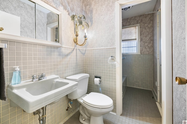 bathroom with tile walls, toilet, a wainscoted wall, tile patterned flooring, and a sink