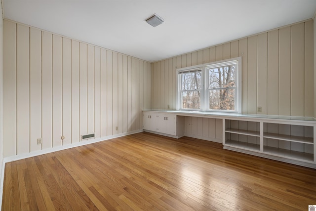 empty room featuring light wood-type flooring, visible vents, baseboards, and built in study area