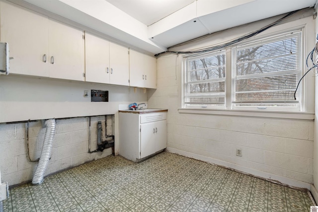 laundry room featuring light floors, plenty of natural light, cabinet space, and concrete block wall