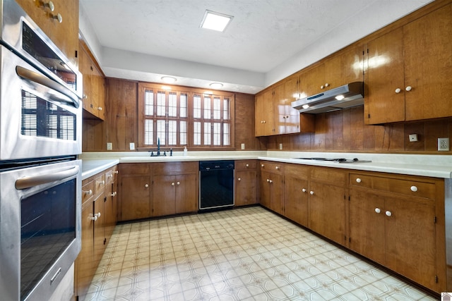 kitchen featuring brown cabinets, light countertops, double oven, dishwasher, and under cabinet range hood