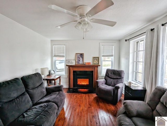 living area with a fireplace with flush hearth, dark wood-style flooring, and a ceiling fan