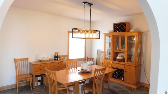 dining space featuring arched walkways, dark tile patterned flooring, and baseboards