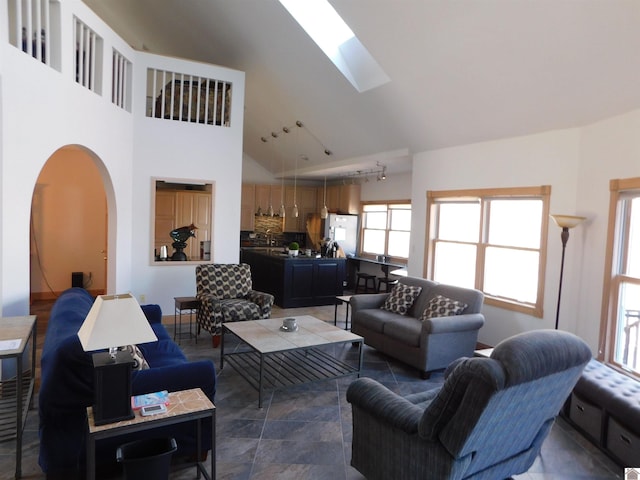 living area featuring arched walkways, high vaulted ceiling, and a skylight