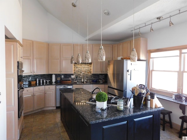 kitchen with light brown cabinets, a sink, appliances with stainless steel finishes, dark stone counters, and a center island with sink