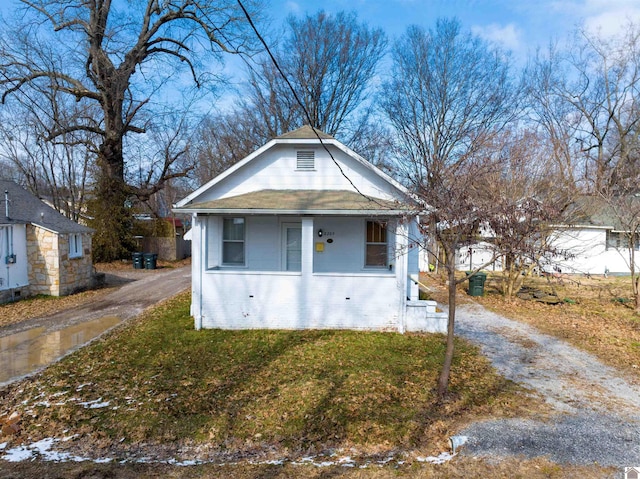 bungalow with driveway, covered porch, a front lawn, and brick siding