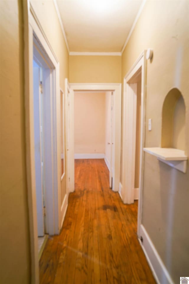 hallway with baseboards, ornamental molding, and wood finished floors