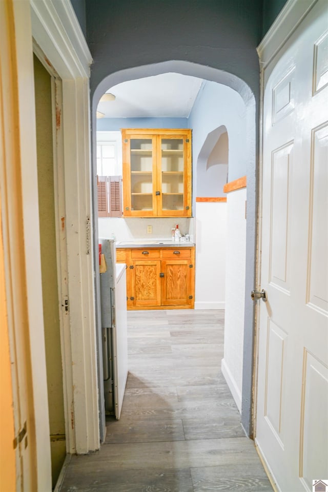 hallway featuring arched walkways, baseboards, and light wood-style floors