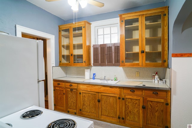 kitchen featuring stove, glass insert cabinets, freestanding refrigerator, light countertops, and a sink