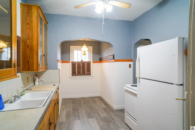 kitchen featuring brown cabinets, glass insert cabinets, light wood-style floors, a sink, and white appliances