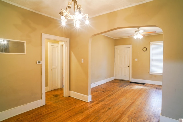 spare room with baseboards, arched walkways, ornamental molding, wood finished floors, and ceiling fan with notable chandelier