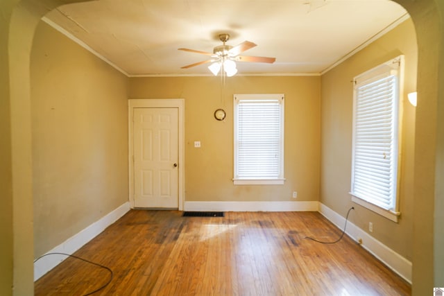 spare room featuring ornamental molding, arched walkways, baseboards, and wood finished floors