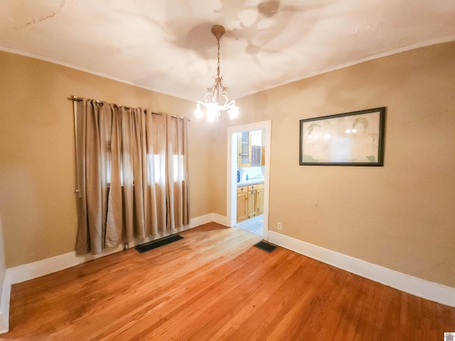 spare room with an inviting chandelier, baseboards, visible vents, and wood finished floors