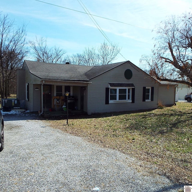 single story home featuring gravel driveway, a shingled roof, and a front lawn