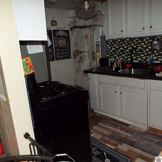 kitchen featuring black stove, decorative backsplash, white cabinets, dark countertops, and a sink