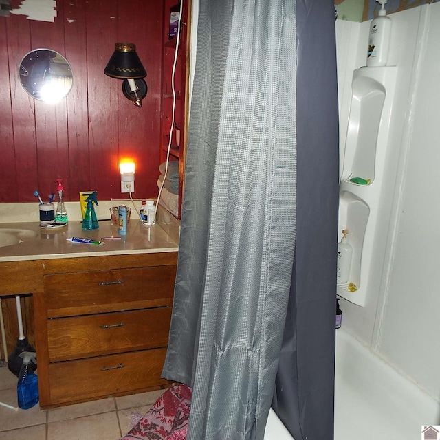 bathroom featuring wooden walls, shower / bath combo with shower curtain, vanity, and tile patterned floors